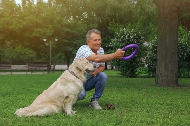 Photo of Happy senior man playing with his Golden Retriever dog in park