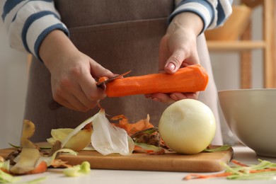 Photo of Woman peeling fresh carrot with knife at table indoors, closeup