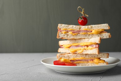 Stack of tasty sandwiches with ham and melted cheese served with tomatoes on grey textured table, closeup. Space for text