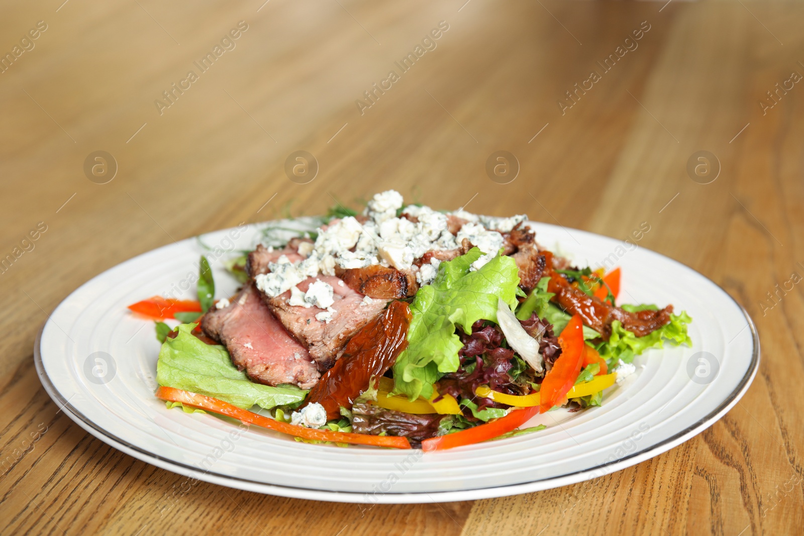 Photo of Delicious salad with roasted meat and vegetables served on wooden table