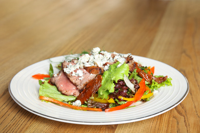 Photo of Delicious salad with roasted meat and vegetables served on wooden table