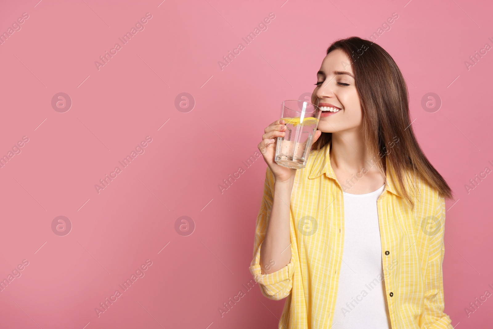 Photo of Young woman drinking lemon water on pink background. Space for text