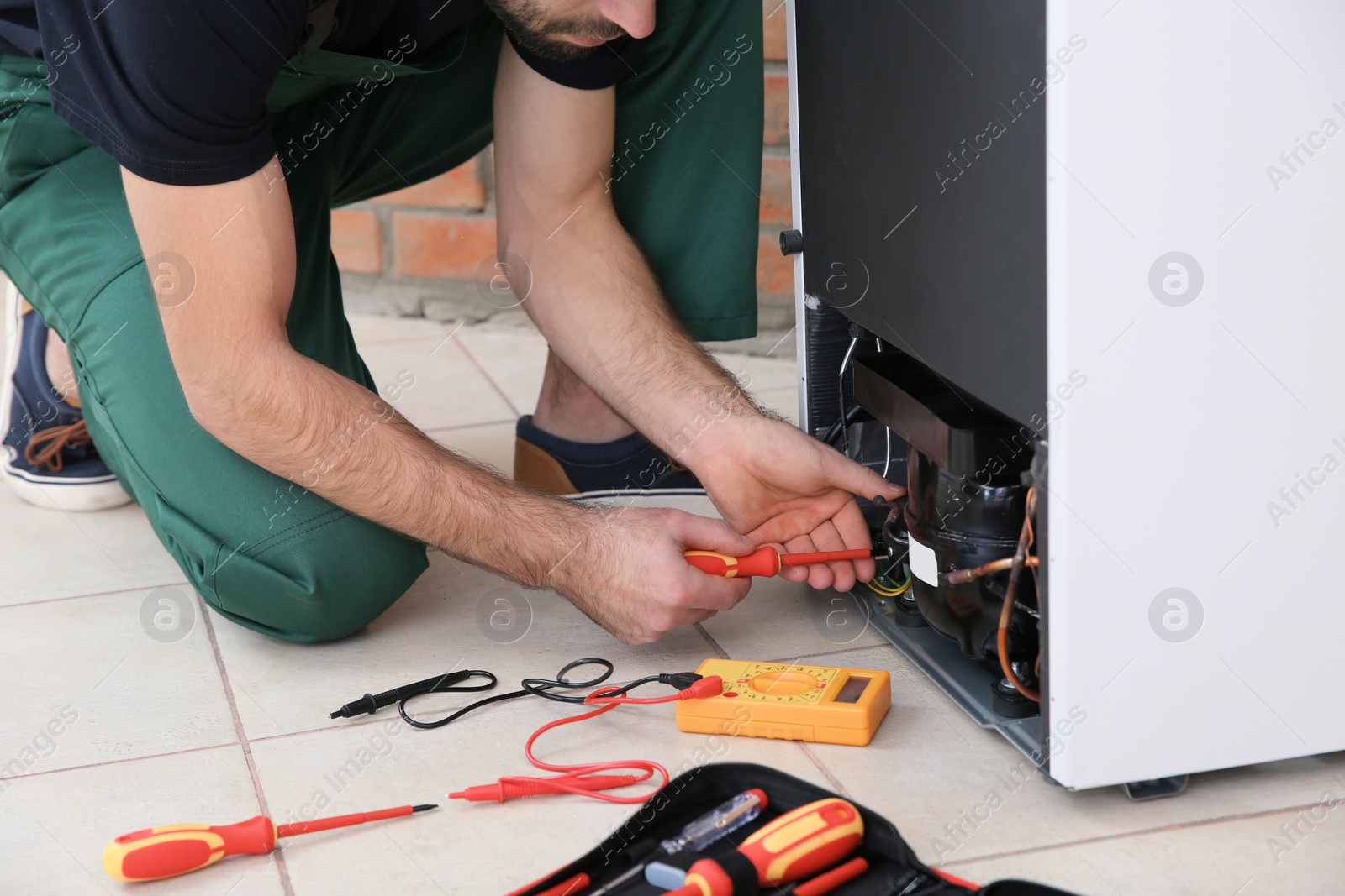 Photo of Male technician repairing broken refrigerator indoors, closeup