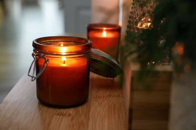Lit candles on wooden table indoors, closeup