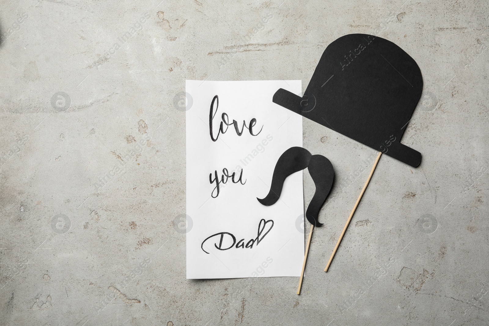 Photo of Note with words LOVE YOU DAD, paper hat and moustache on grey background, flat lay