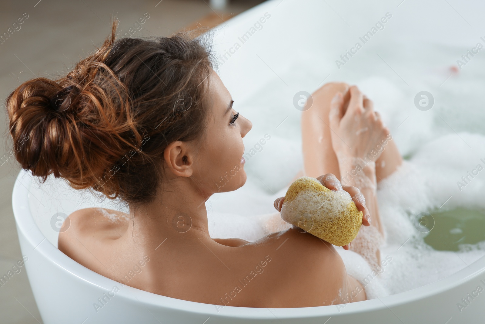 Photo of Beautiful woman with sponge taking bubble bath