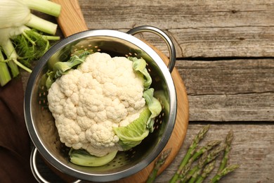 Metal colander with cauliflower, fennel and asparagus on wooden table, flat lay