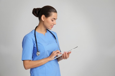 Portrait of young medical assistant with stethoscope and tablet on color background. Space for text