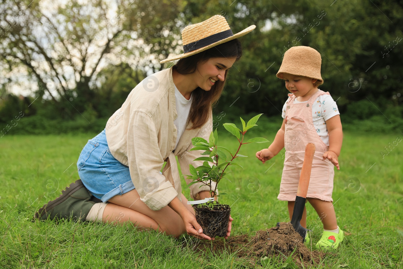 Photo of Mother and her baby daughter planting tree together in garden