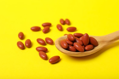 Photo of Wooden spoon with pills on yellow background, closeup. Anemia treatment