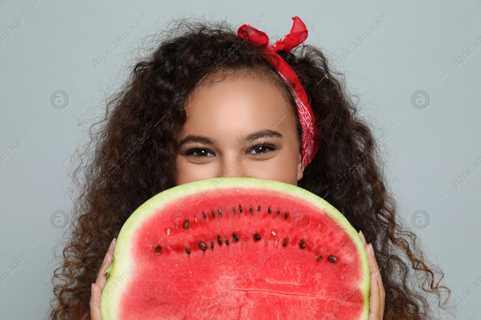 Photo of Beautiful young African American woman with half of watermelon on grey background