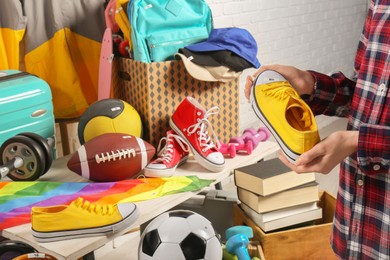 Photo of Woman holding sneaker near many different stuff indoors, closeup. Garage sale