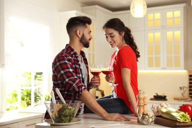 Lovely young couple drinking wine while cooking together at kitchen