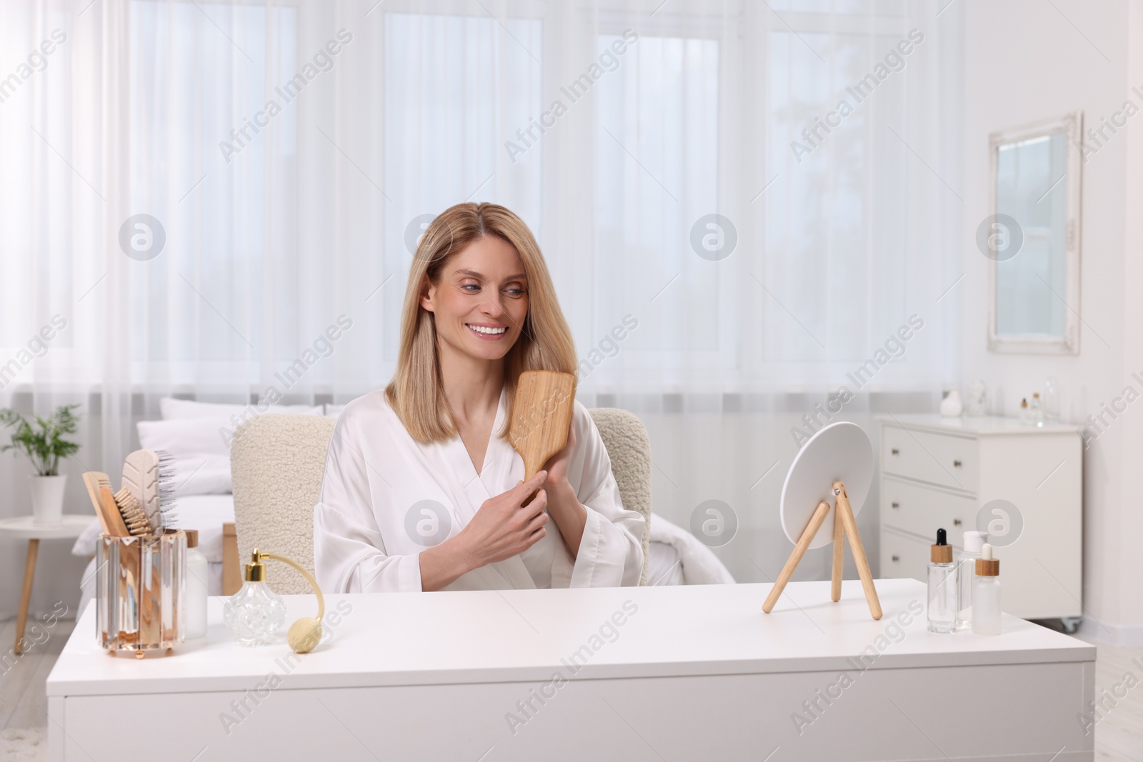Photo of Beautiful woman brushing her hair at vanity in bedroom