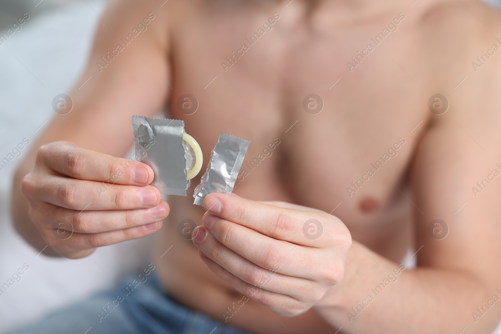 Photo of Closeup of man holding open pack with condom on bed