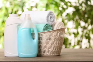 Photo of Basket with clean towels and detergents on table against blurred background. Space for text