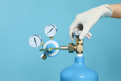 Photo of Medical worker checking oxygen tank on light blue background, closeup