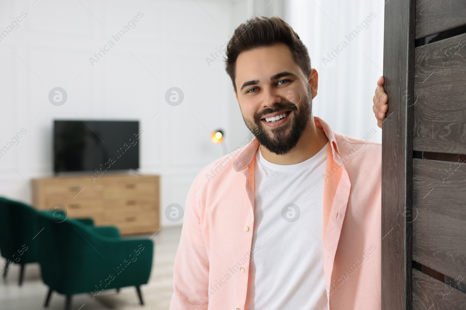 Photo of Happy man standing near door, space for text. Invitation to come indoors