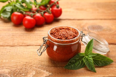 Photo of Delicious adjika sauce in glass jar with basil on wooden table