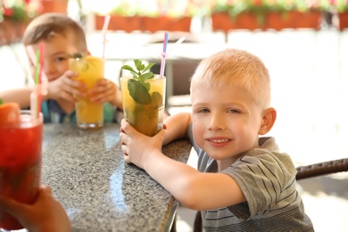 Photo of Cute children with natural lemonade at table in cafe