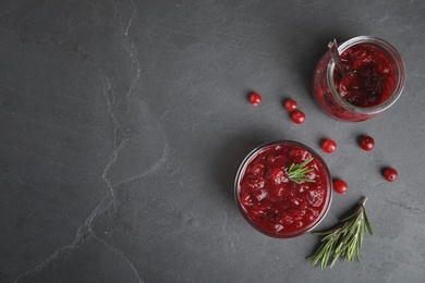 Photo of Jar and bowl of cranberry sauce with rosemary on grey background, flat lay. Space for text