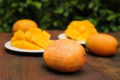 Delicious ripe whole and cut mangos on wooden table outdoors