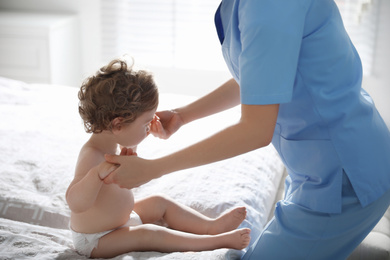 Orthopedist examining little baby on bed indoors