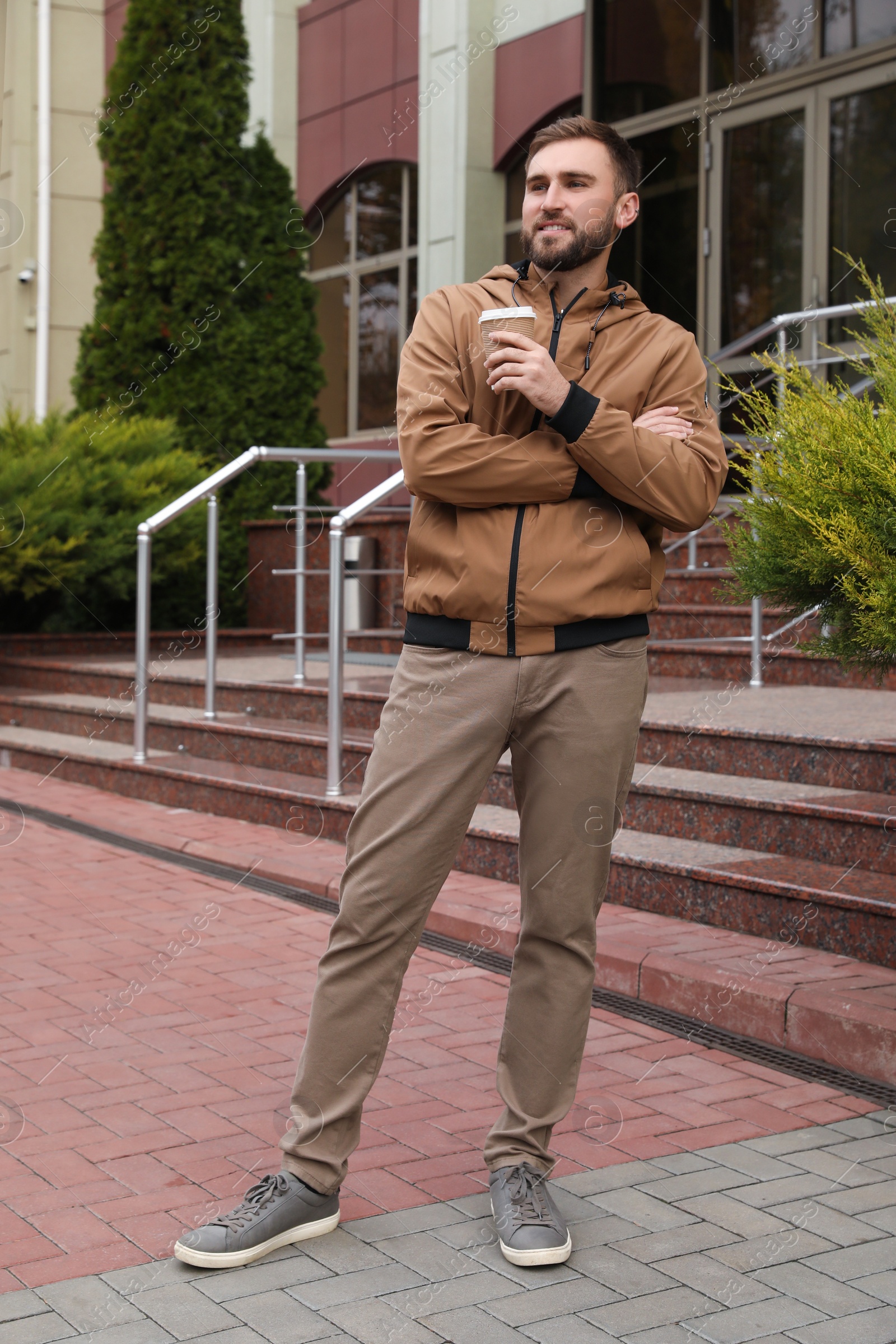 Photo of Handsome man wearing stylish clothes with cup of coffee on city street. Autumn walk