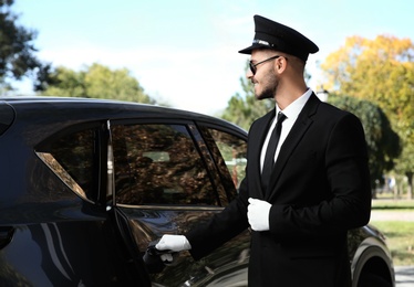 Photo of Young handsome driver opening luxury car door. Chauffeur service