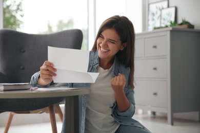Excited woman reading paper letter at home