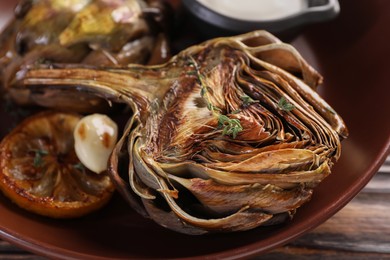 Photo of Tasty grilled artichoke in bowl on table, closeup