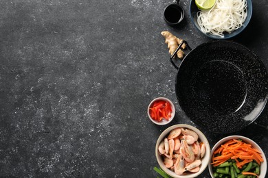 Flat lay composition with black wok and products on dark textured table. Space for text