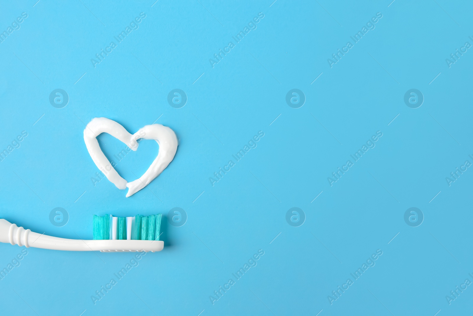 Photo of Heart made with toothpaste and brush on light blue background, top view. Space for text
