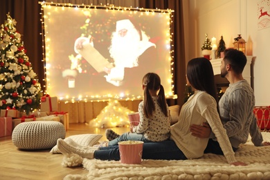 Photo of Family watching movie on projection screen in room decorated for Christmas. Home TV equipment