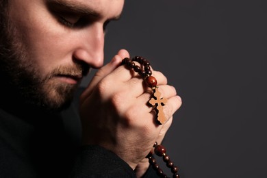 Photo of Priest with rosary beads praying on dark background, closeup