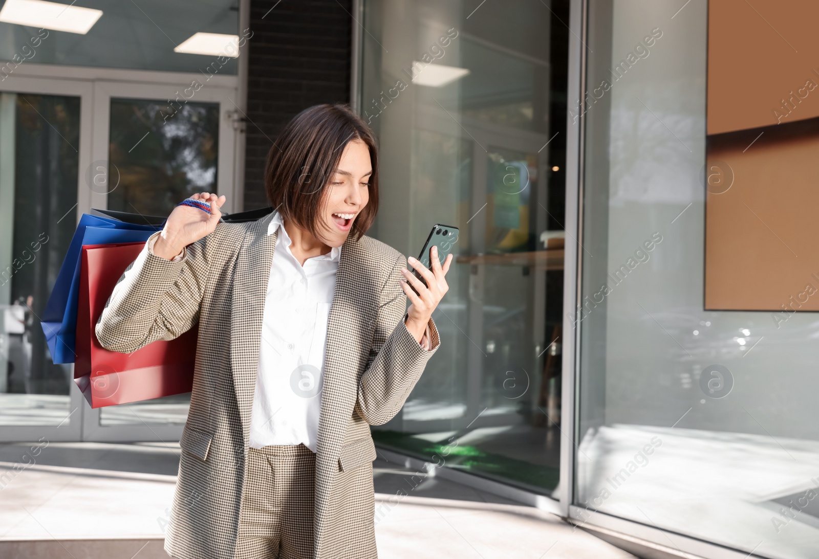 Photo of Special Promotion. Emotional young woman with shopping bags and smartphone on city street