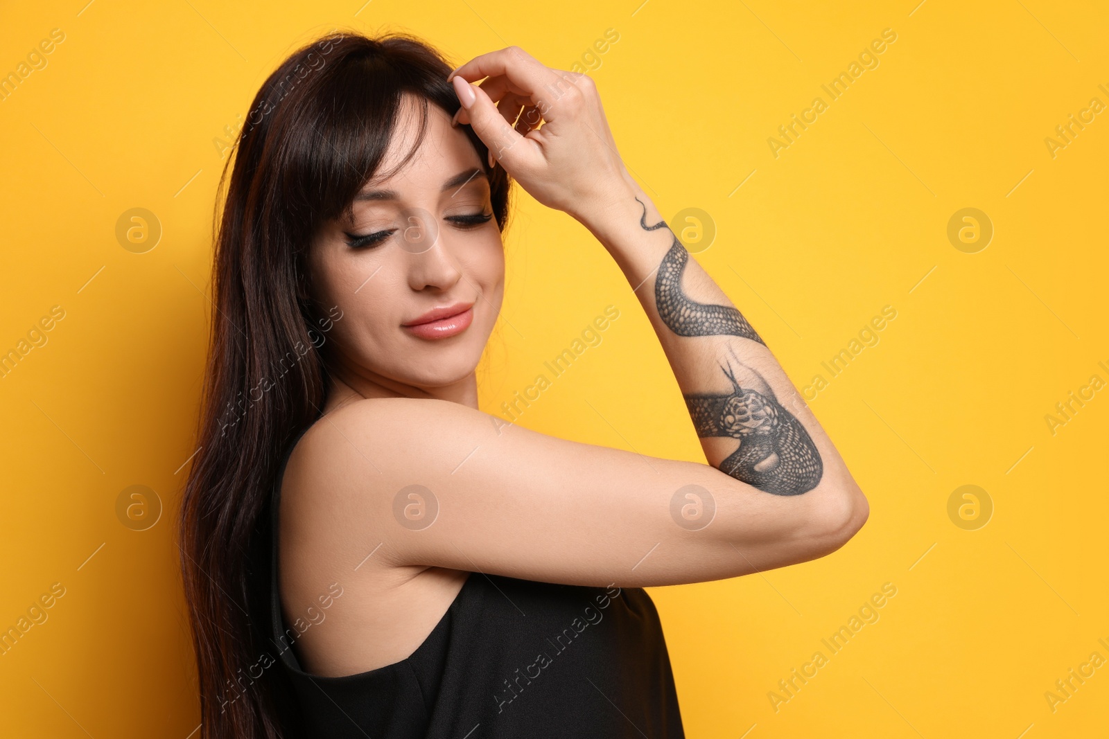 Photo of Beautiful woman with tattoos on arm against yellow background