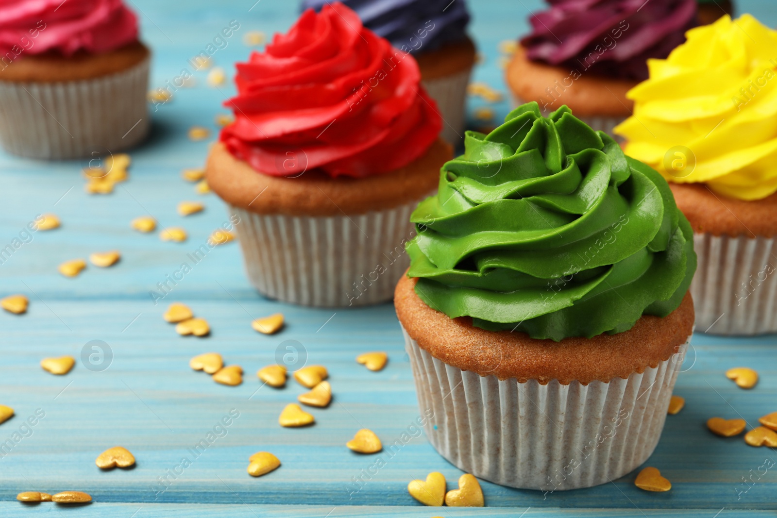 Photo of Delicious colorful cupcakes and heart shaped sprinkles on light blue wooden table, closeup. Space for text