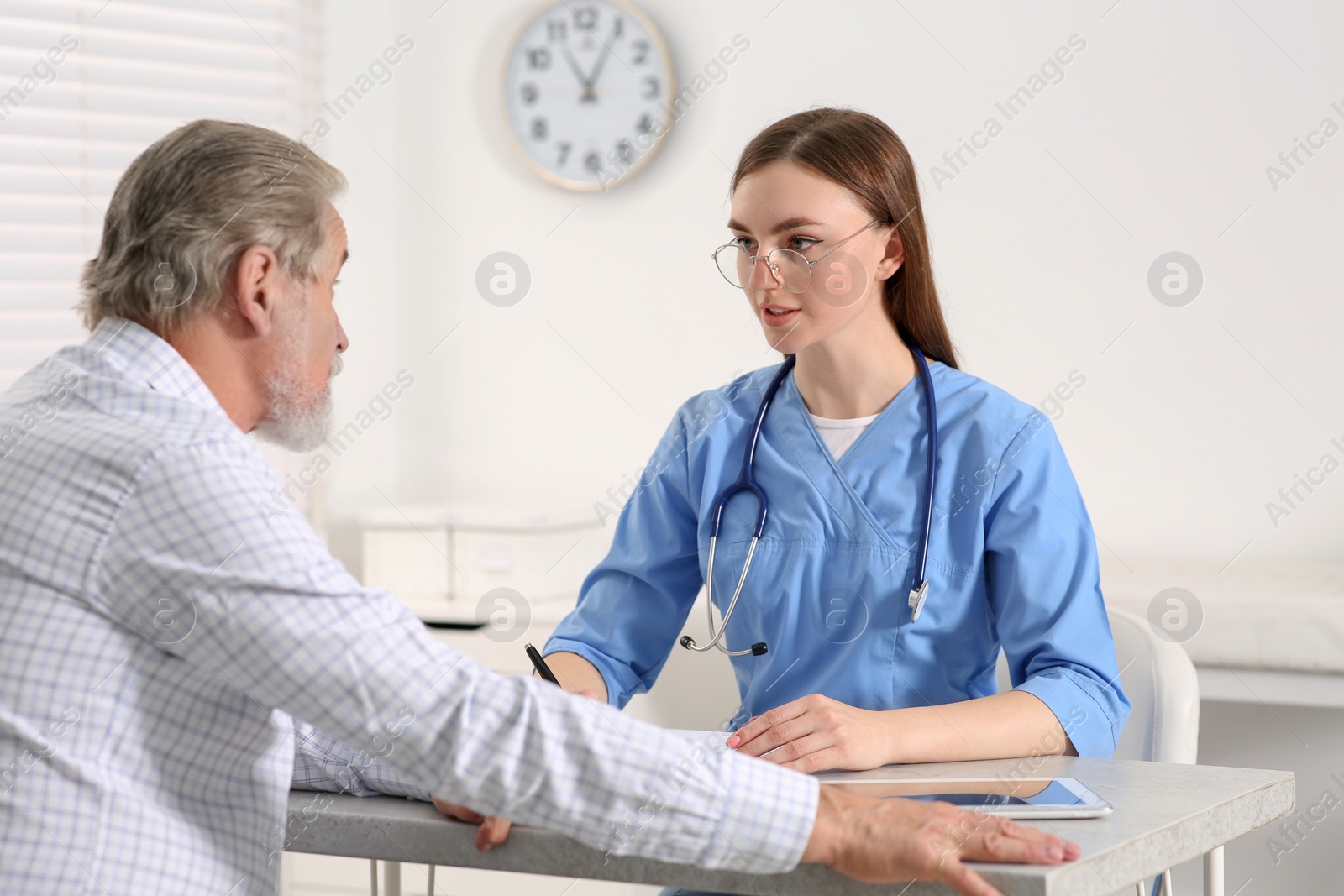 Photo of Doctor filling patient's medical card at table in clinic