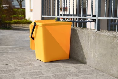 Photo of Yellow trash bin near fence outdoors on sunny day