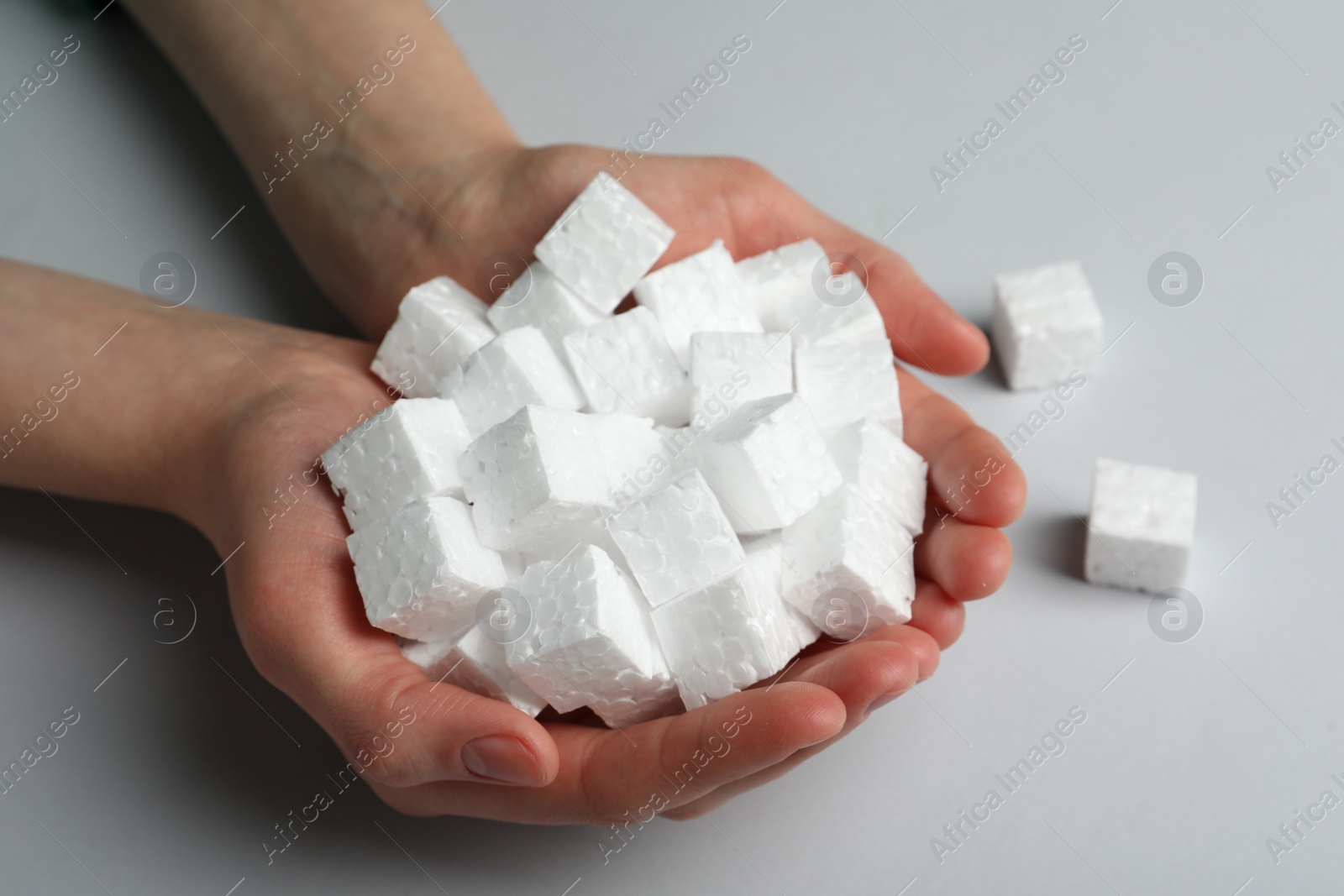 Photo of Woman with handful of styrofoam cubes on light grey background, closeup
