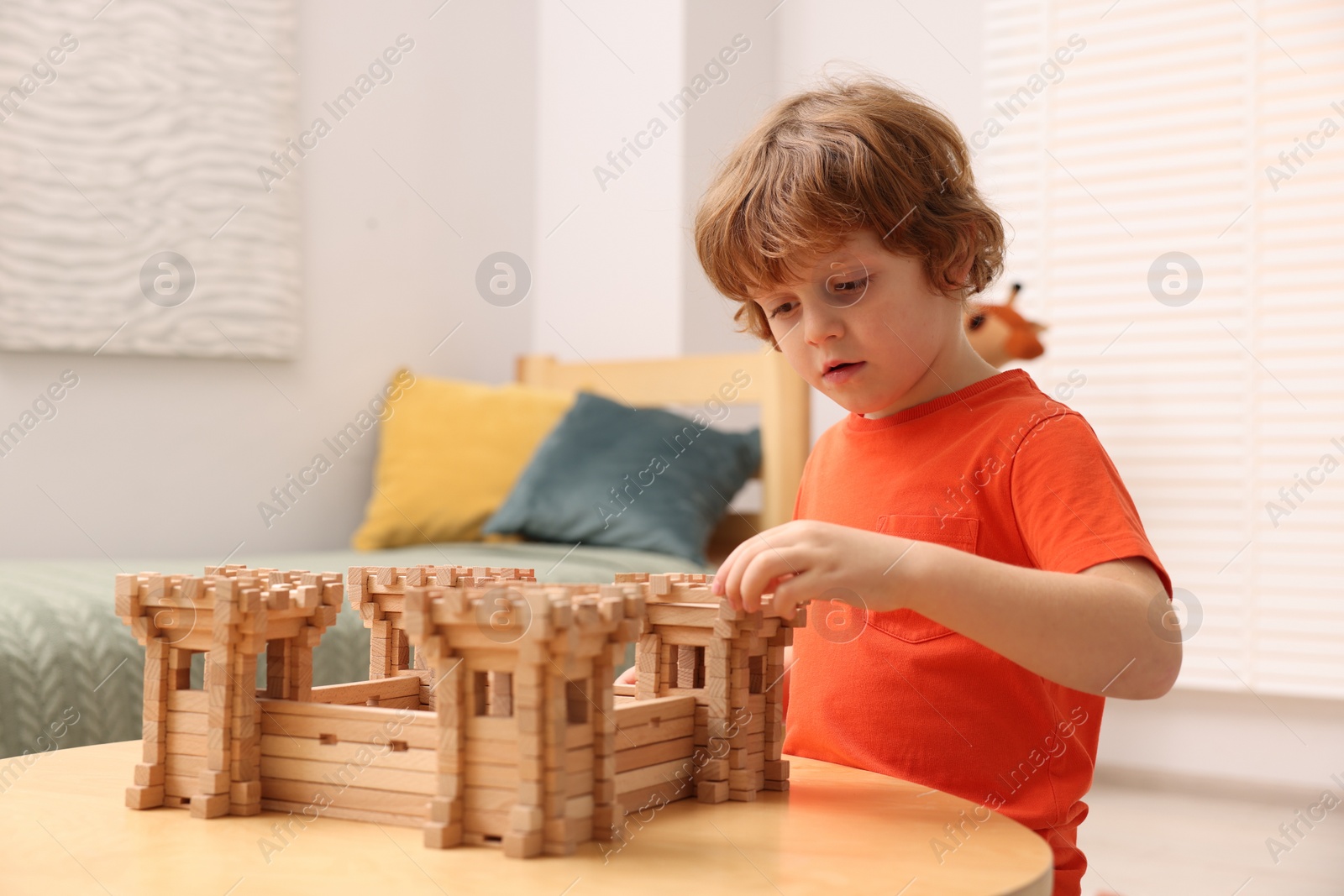 Photo of Cute little boy playing with wooden fortress at table in room. Child's toy