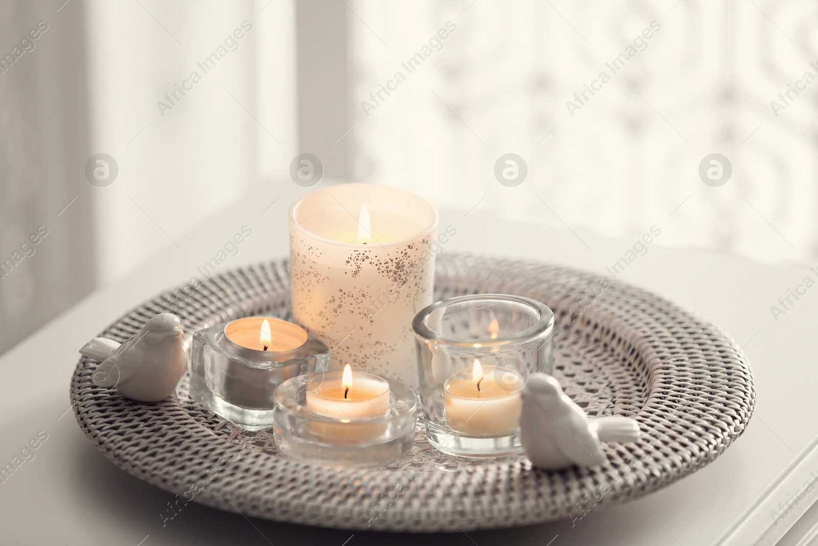 Photo of Beautiful burning candles on tray against light background