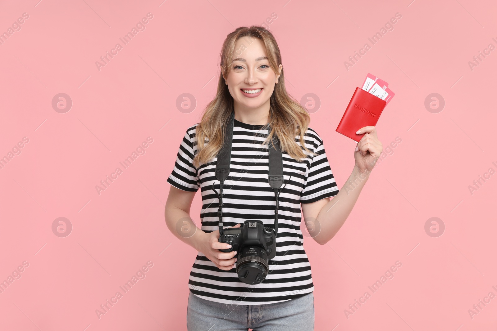 Photo of Happy young woman with passport, ticket and camera on pink background