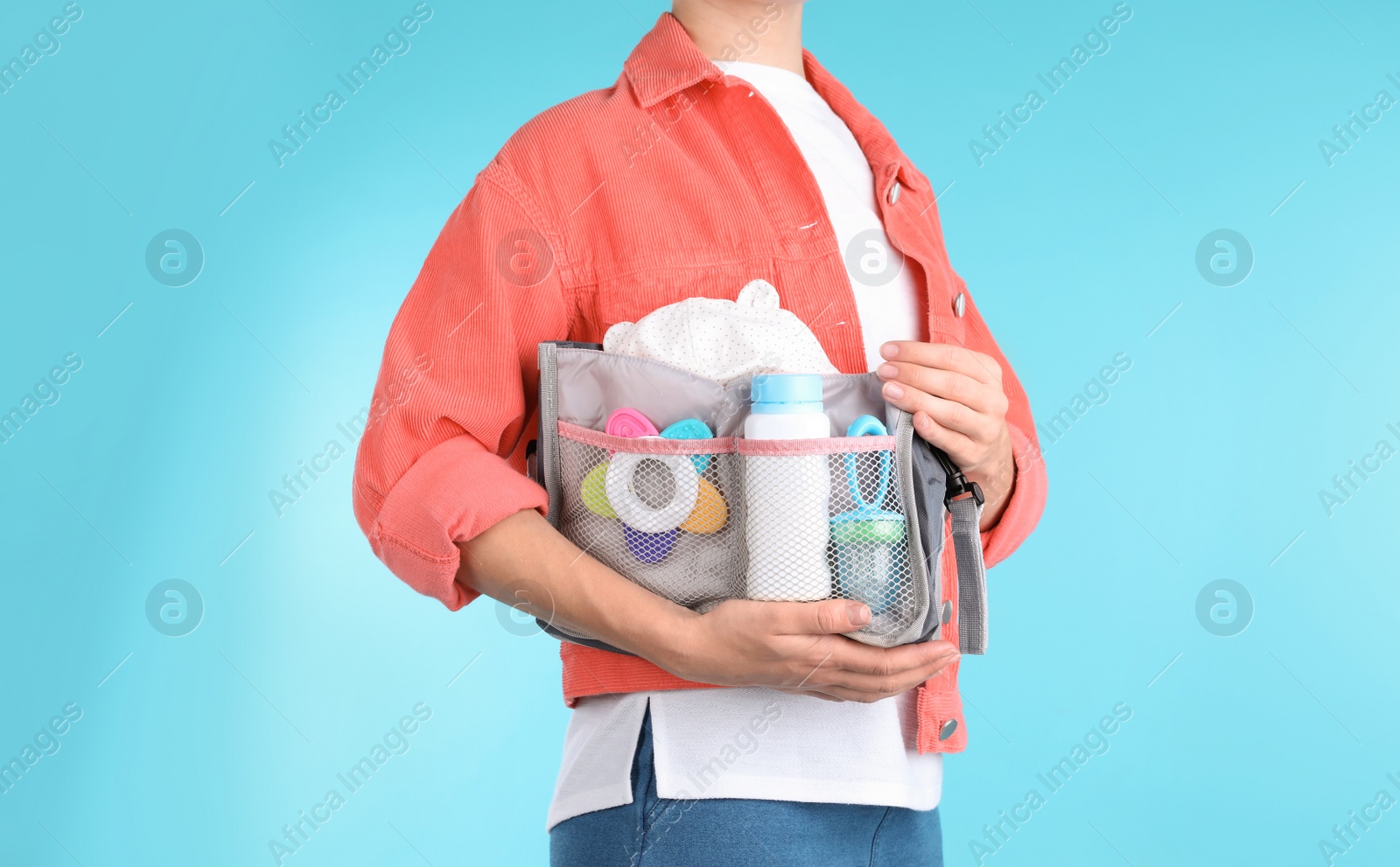 Photo of Woman holding maternity bag with baby accessories on color background, closeup