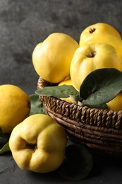 Photo of Fresh ripe organic quinces with leaves in wicker basket on table, closeup