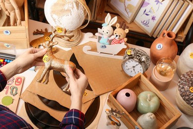 Photo of Woman holding toy deer near table with many different stuff, above view. Garage sale