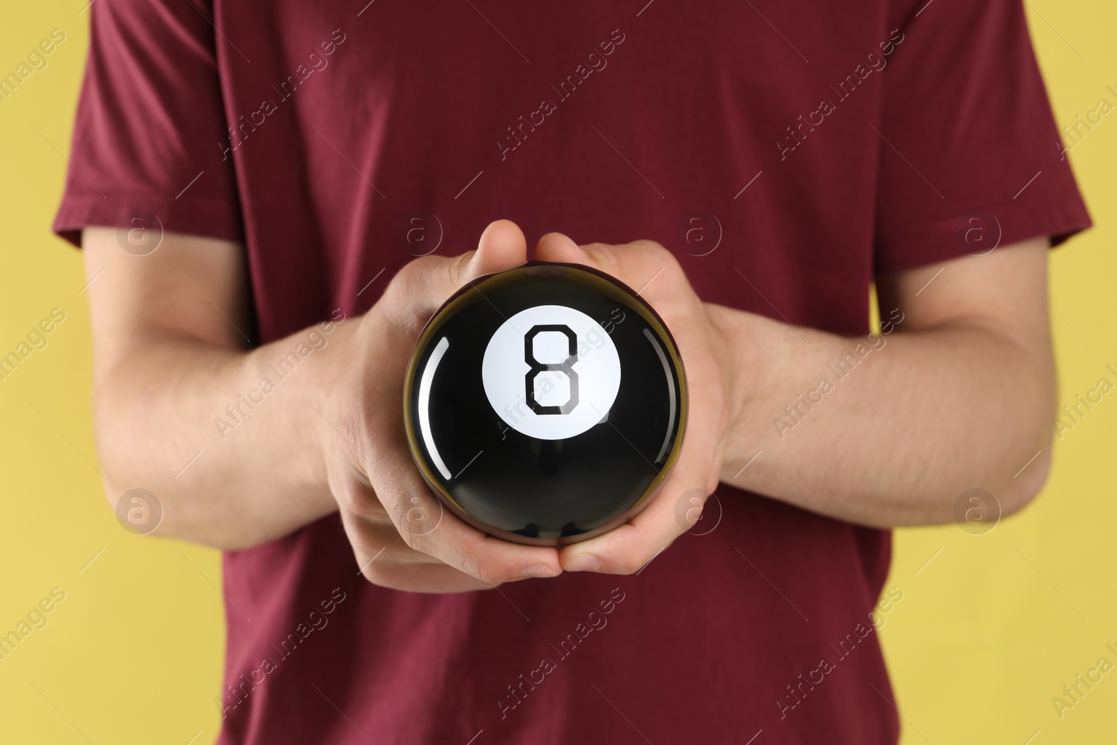 Photo of Man holding magic eight ball on yellow background, closeup