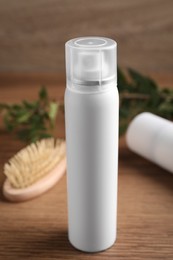 Dry shampoo spray near hairbrush on wooden table, closeup