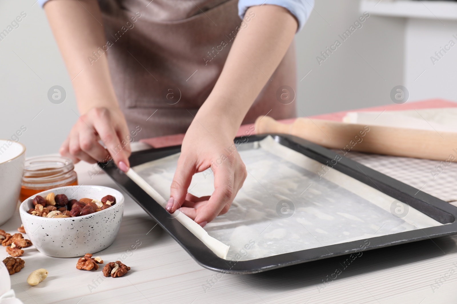 Photo of Woman making delicious baklava at white wooden table, closeup